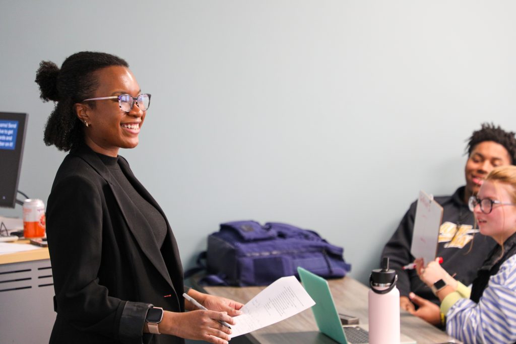 Dr. Nadhira Hill stands smiling in front of a class of students
