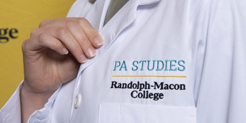 A PA student shows off their white coat, with the words 'PA Studies' embroidered.