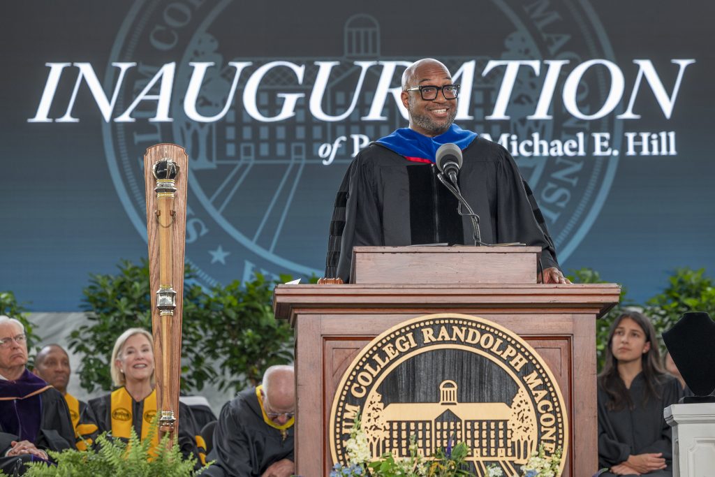 Poet Kwame Alexander stands and smiles at the podium on the stage of the inauguration of Michael Hill