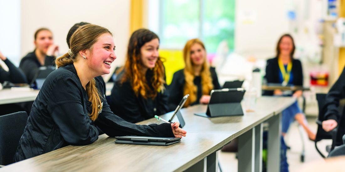 RMC Nursing students in scrubs laugh inside of a classroom