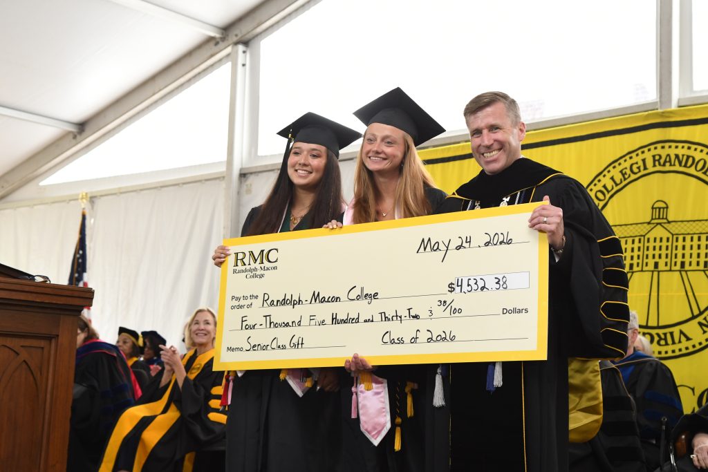 President Hill, Malori Brown, and Maddy Sayasithsena hold a check representing the senior class gift on the Commencement stage