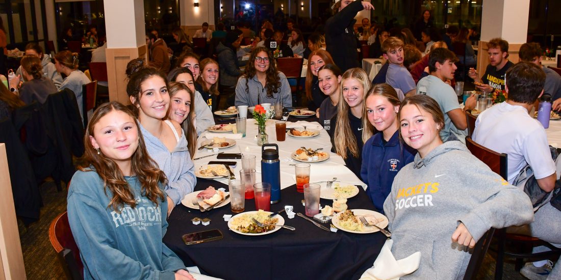 Students pose at a table in Estes Dining Hall with plates of food visible.