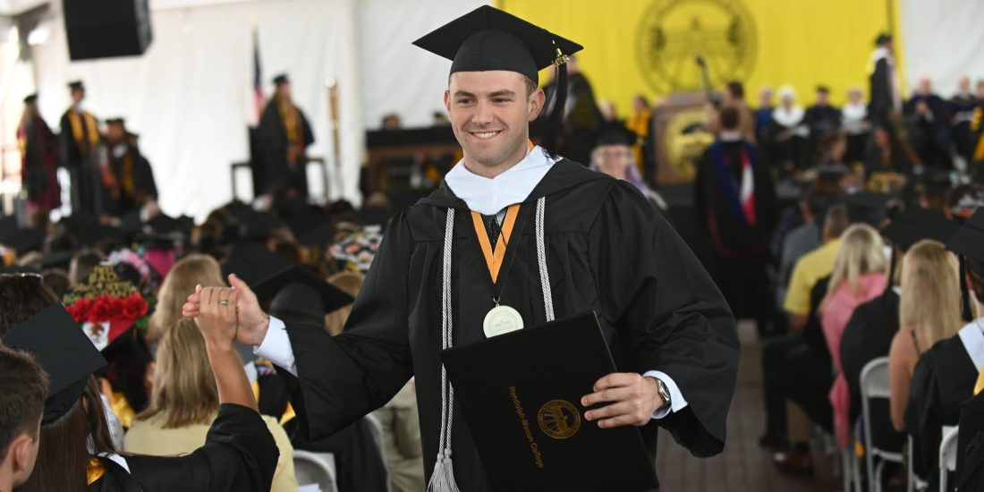 A graduate high-fives a classmate after walking off the 2026 Commencement stage holding a diploma