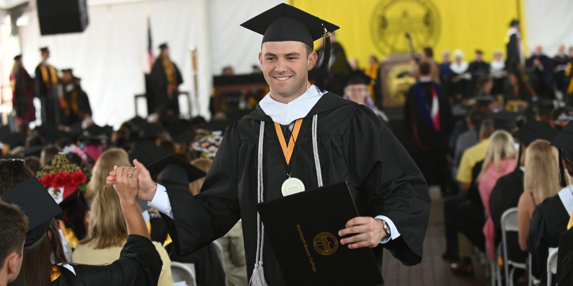 A graduate high-fives a classmate after walking off the 2026 Commencement stage holding a diploma