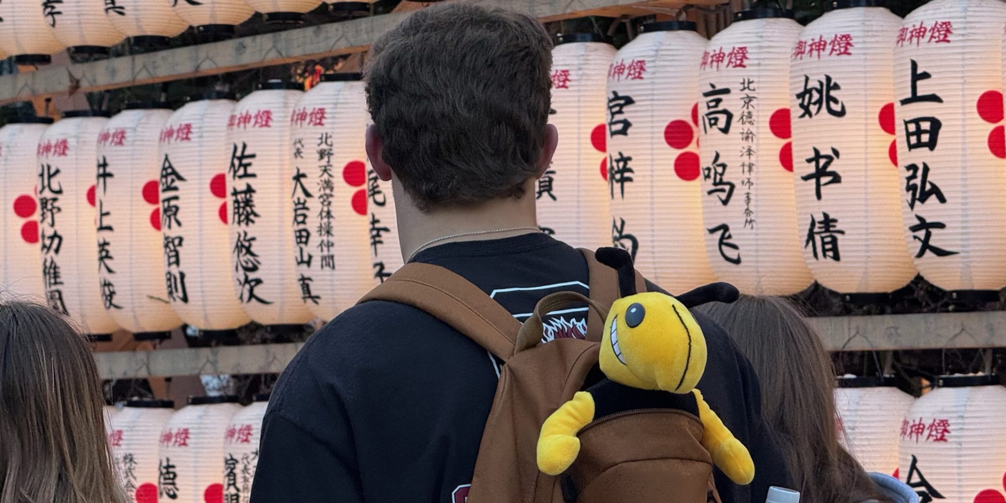 A student looks at a wall of paper lanterns during a study abroad trip to Japan, while a plush Buzz sticks out of his backpack