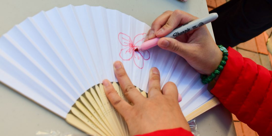 A student draws a pink flower on a traditional Japanese fan