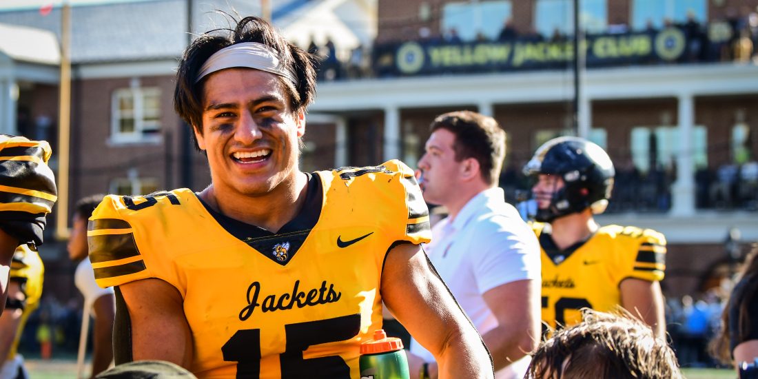 RMC football player stands on football field and smiles for the camera.