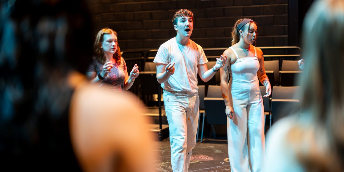 A group of RMC students stand in a circle, participating in acting warmup exercises.