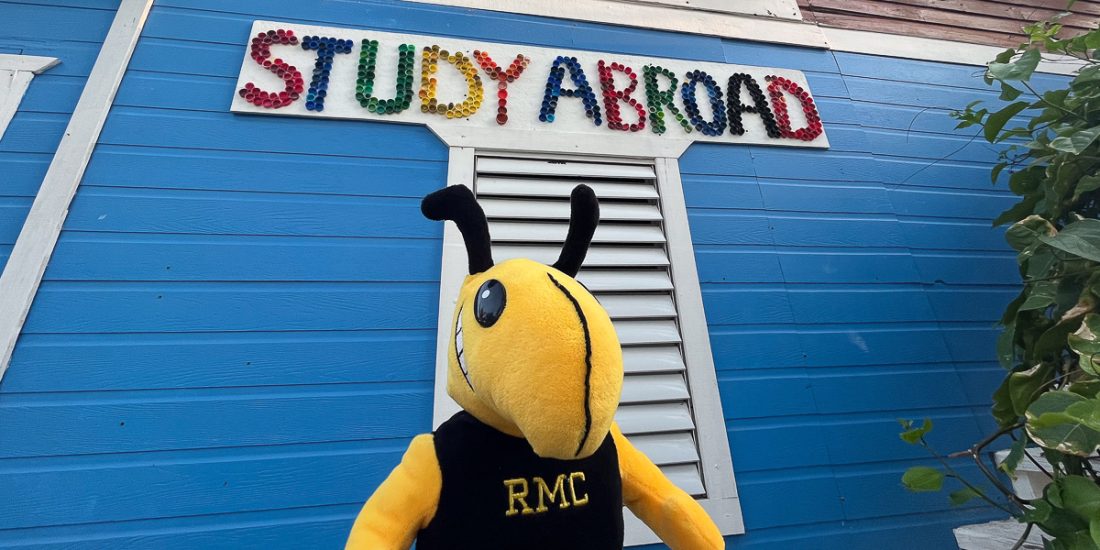 Student holds stuffed Buzz in front of sign that reads 'Study Abroad'
