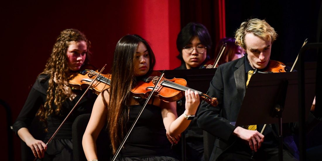Students playing viola on a stage during a concert.