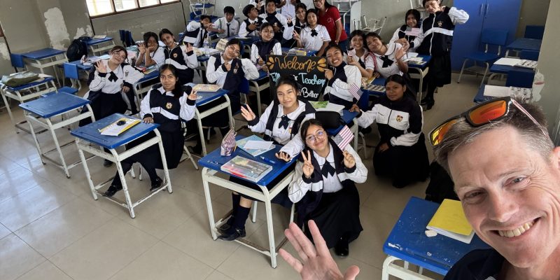 A selfie taken by a teacher in front of a class of Peruvian students waving and holding American flags