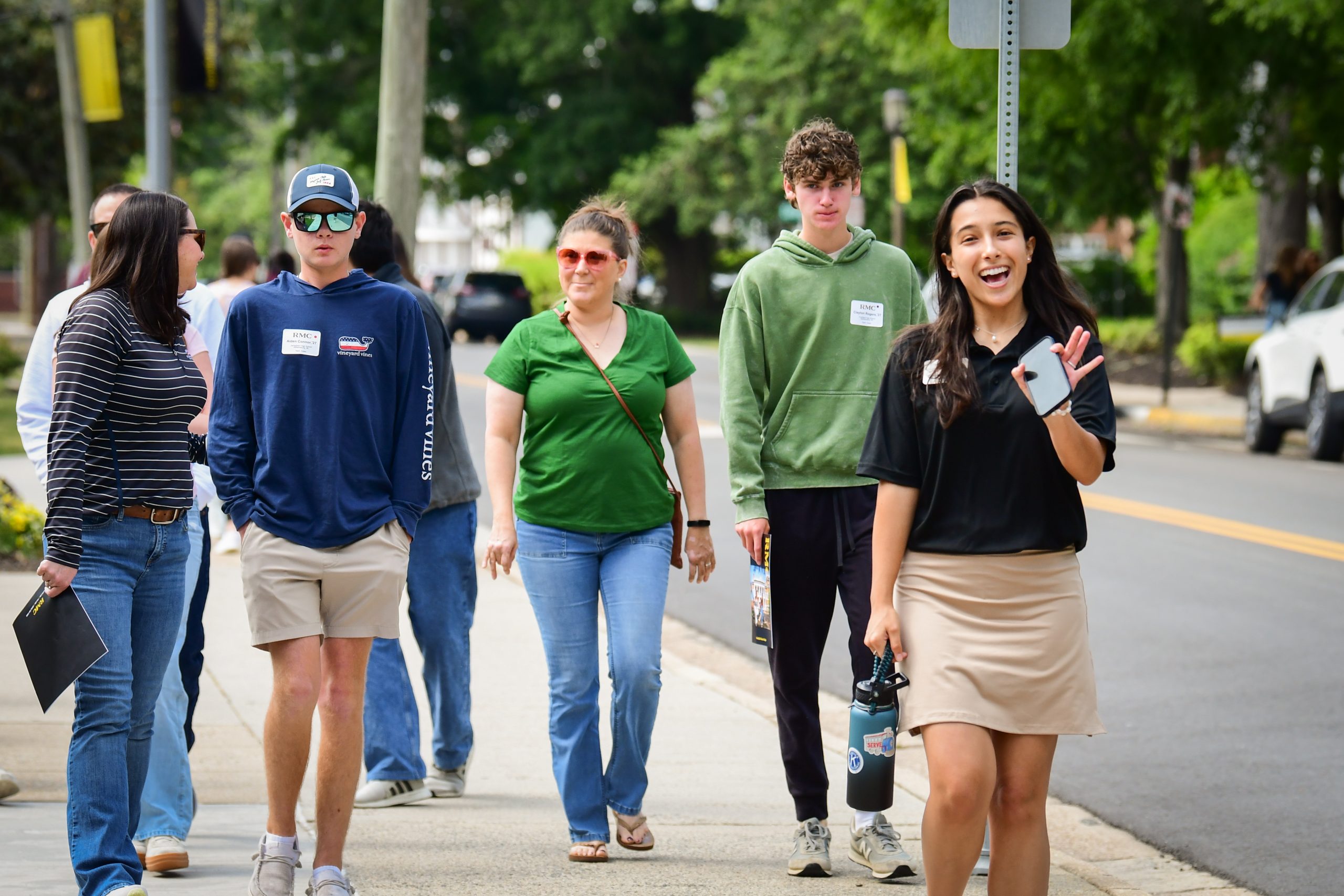Prospective students tour campus with a guide, who smiles and waves at the camera.