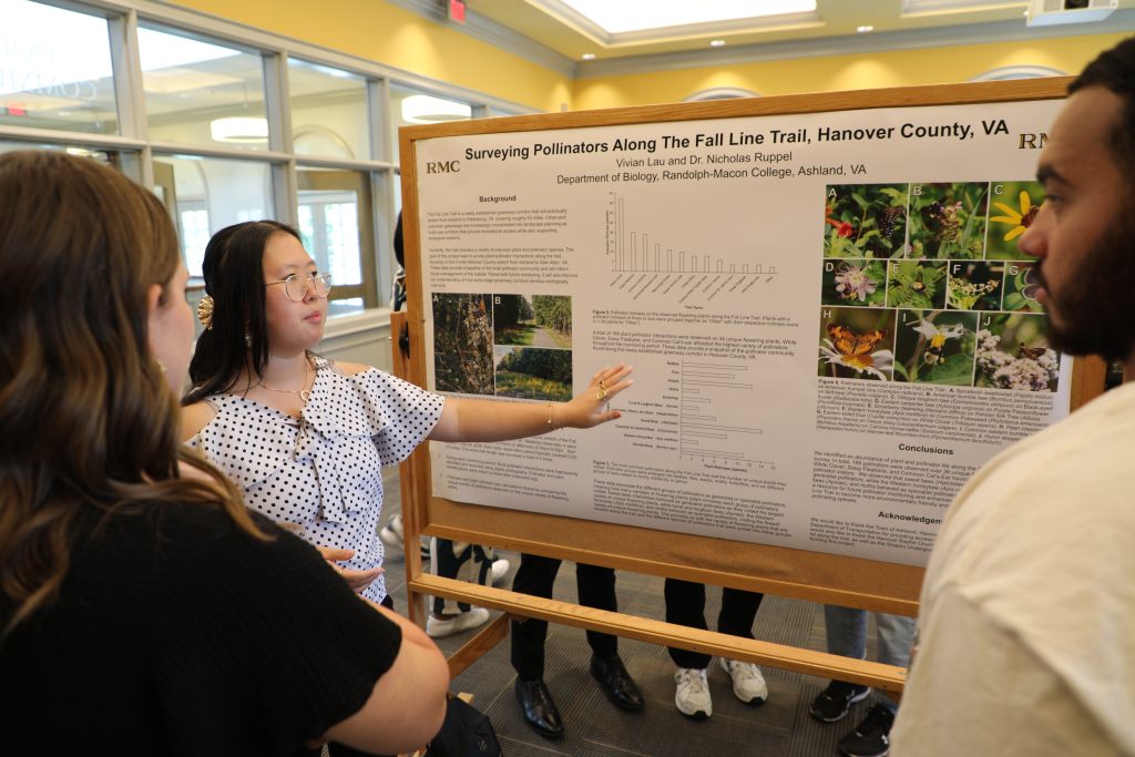 A student explains her poster on pollinators to two people during the 2026 SURF Symposium