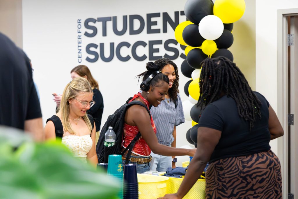 Students smile and talk under Center for Student Success sign at event