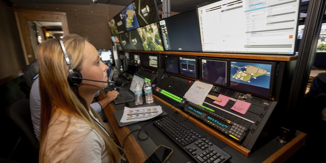 Emma Landis wears a headset inside a Fox Sports production truck, working on graphics during a broadcast