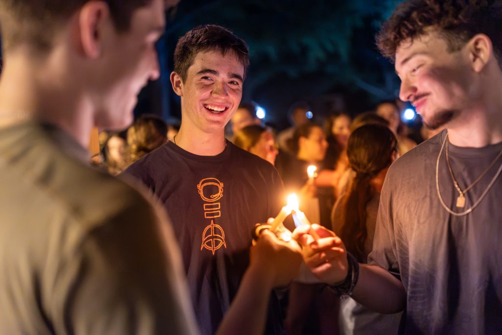 Three students hold candles together during a nighttime ceremony