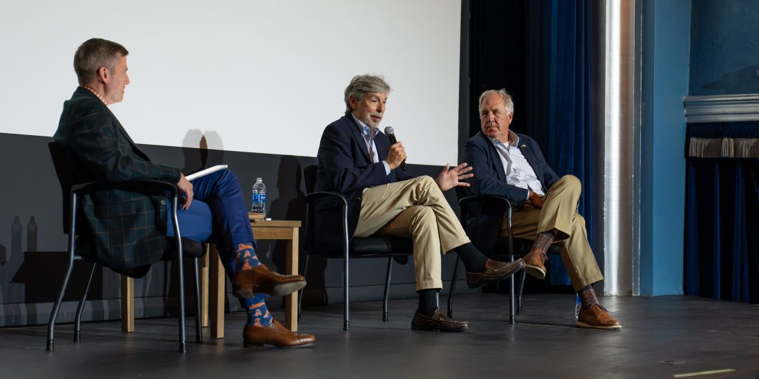 President Michael Hill sits on stage next to two former congressmen, including one holding a microphone