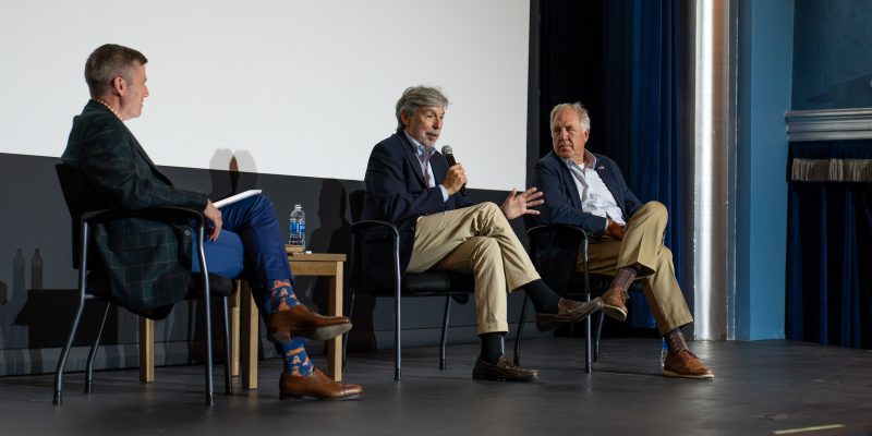 President Michael Hill sits on stage next to two former congressmen, including one holding a microphone
