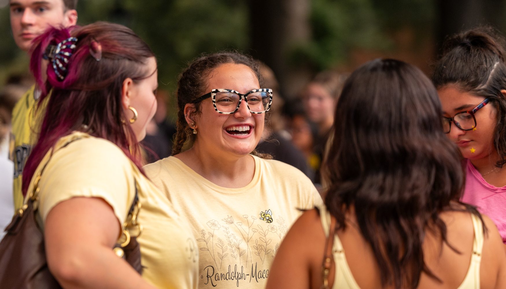 Three students, one in RMC swag. smile and laugh during a conversation.