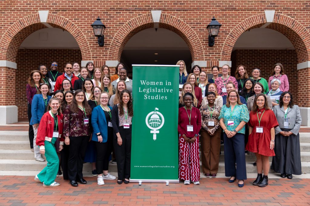 A large group of women pose for a photo on the steps of Birdsong Hall with a "Women in Legislative Studies" banner