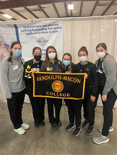 Nursing students at R-MC hold a College banner and pose at the pop-up health clinic that they had been volunteering at.