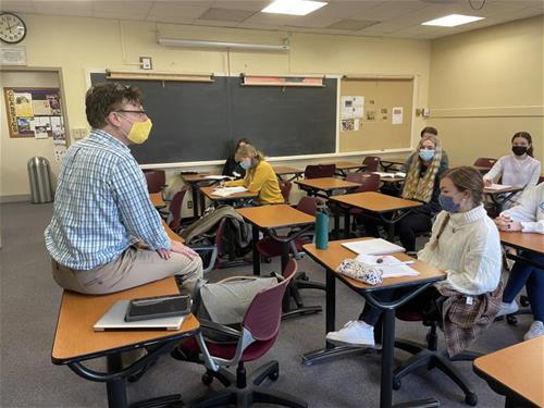 Dr. Benjamin Huff sits on a desk while giving a lecture to students in his Trust and Social Cohesion class.