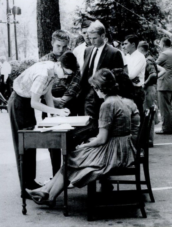 A black-and-white photo of students lining up to sign the registrar's Matriculation book